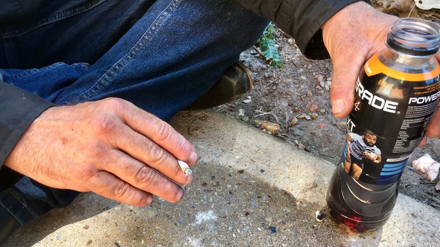 A man's hands holding a cigarette and a plastic drink bottle filled with dark liquid