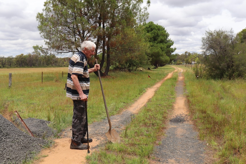 George collis sands with a walking stick and shovel looking down at his driveway