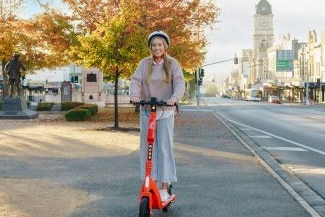 A girl riding an orange e-scooter down a street