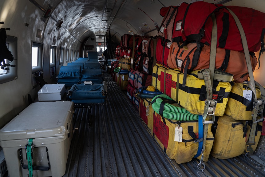 The inside of a plane with colourful bags stacked up one side.