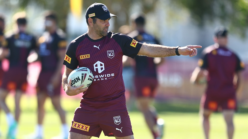A Queensland State of Origin coaching staff member holds a ball as he points on the field during a training session.