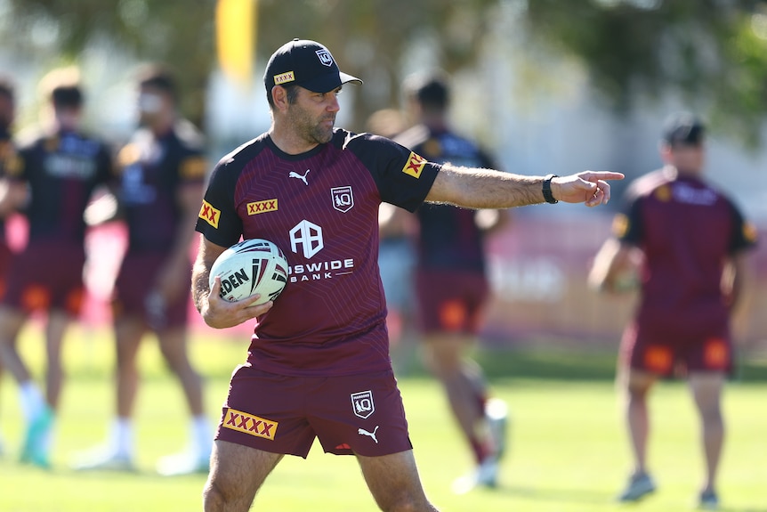 A Queensland State of Origin coaching staff member holds a ball as he points on the field during a training session.