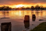 The sun sets over a residential area on the edge of a swollen waterway.
