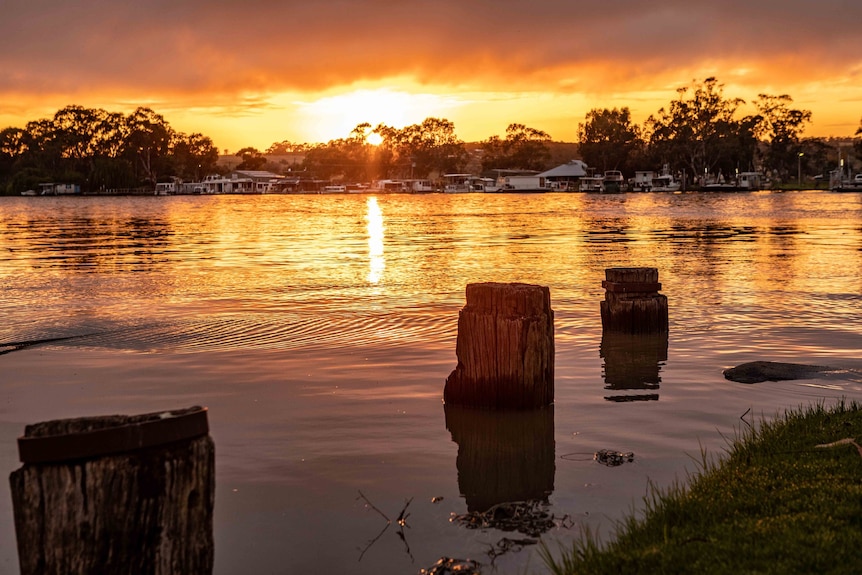 The sun sets over a residential area on the edge of a swollen waterway.
