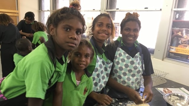 Four Aboriginal girls in green school uniform kneading dough and smiling