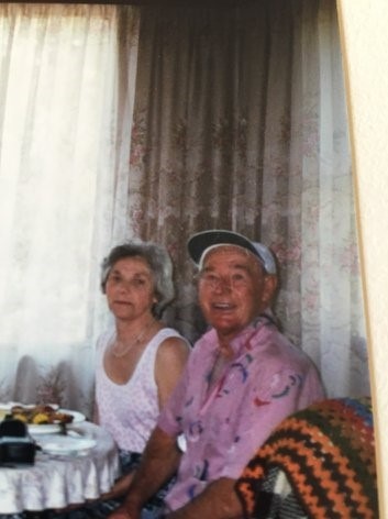 An older woman in a white singlet sitting next to an elderly man in a pink shirt and white cap.