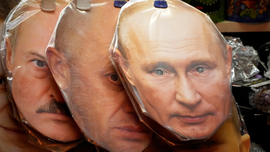 Three flat face masks wrapped in plastic are hung from a string, showing Putin in front, Prigozhin and Lukashenko behind