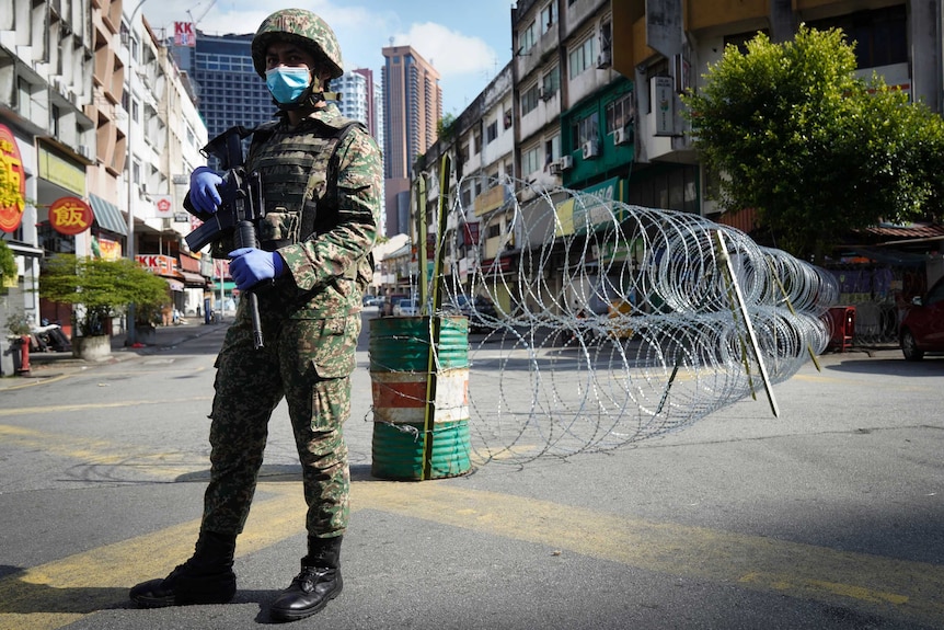 A soldier wearing a face mask stands guard near barbed wire in Kuala Lumpur.