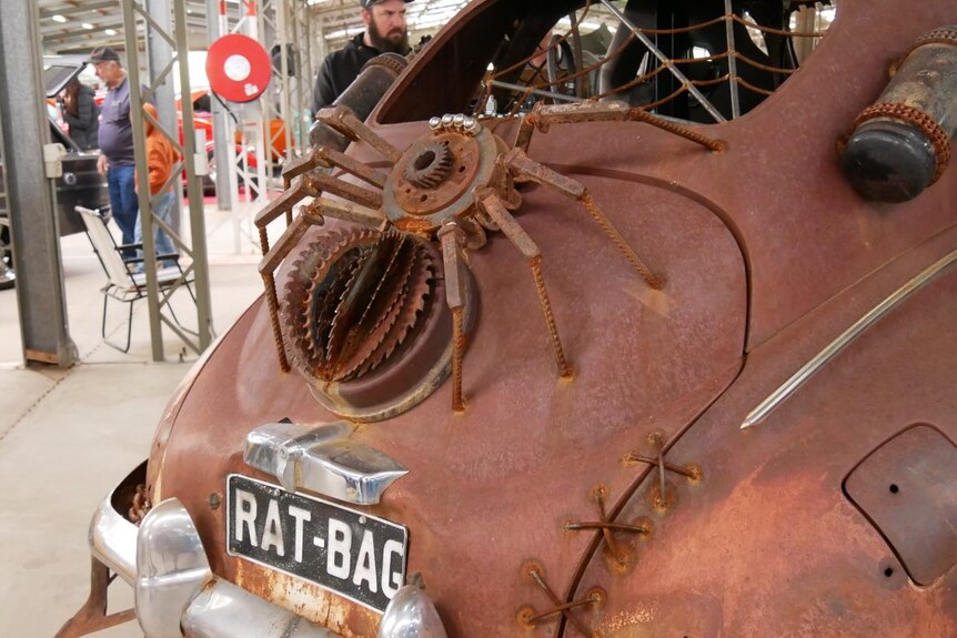 A brown, rusty vehicle has the words 'rat bag' on the number plate.