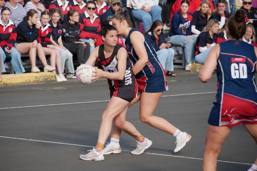 A netball player holds the ball away from a defender. 