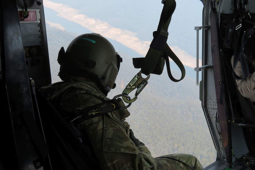 A person in army uniform framed by an open helicopter window.