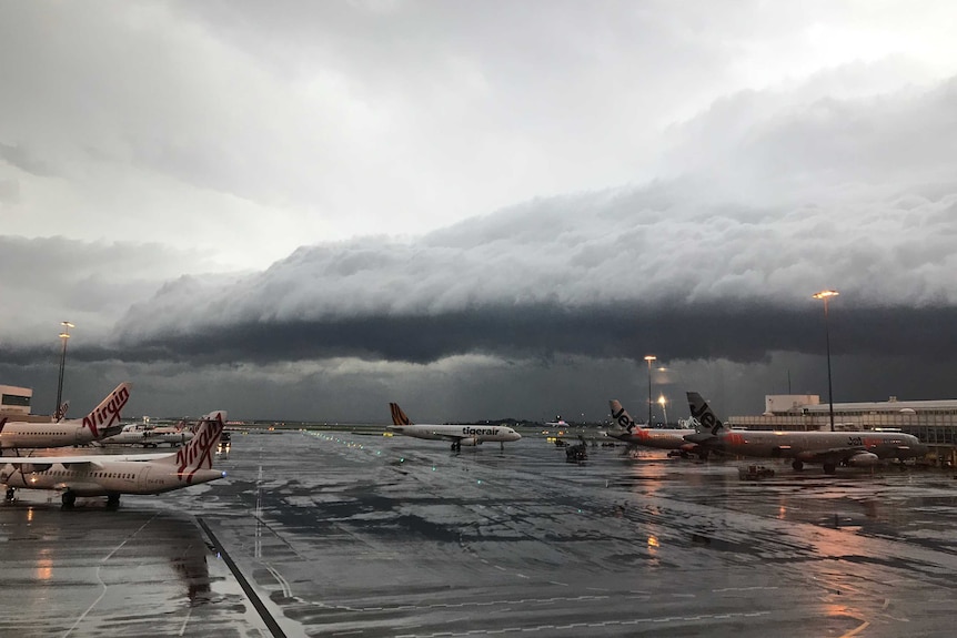 A mushroom-shaped storm cloud looms over planes on the tarmac.