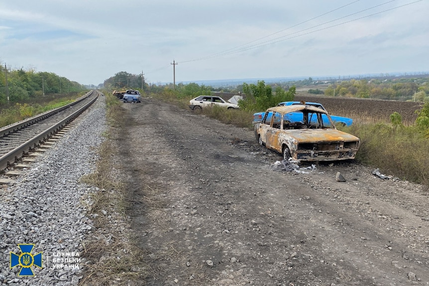 Three charred cars seen beside railway line.