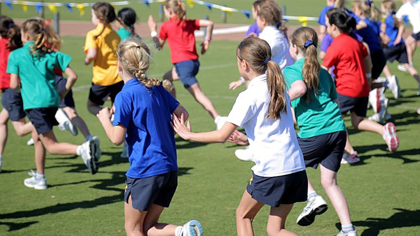Girls in coloured faction shirts pictured from behind in a running race.