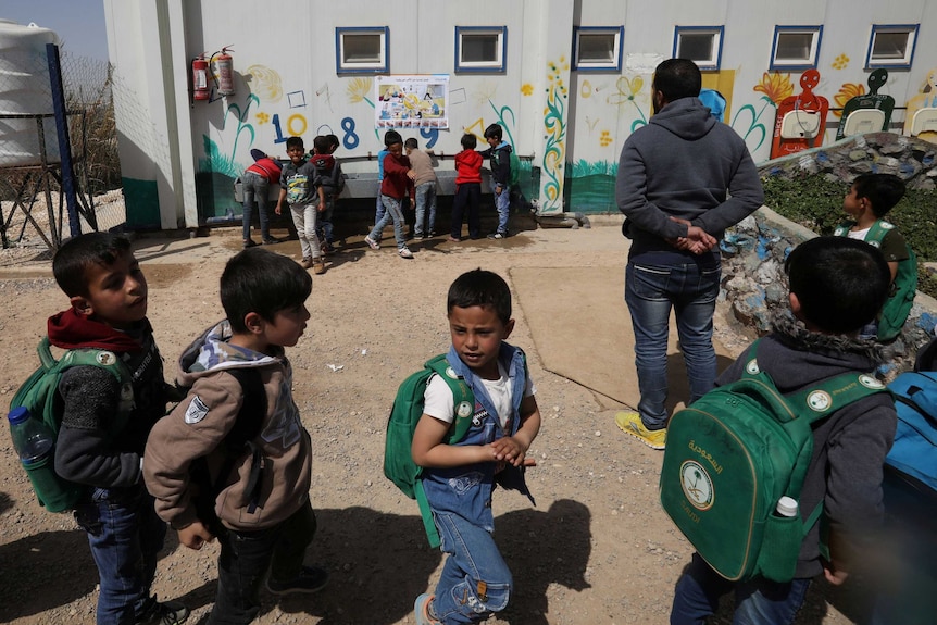 A group of children line up to wash their hands at an outdoor sink