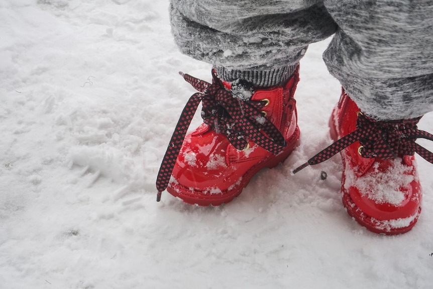A child wears red boots in the snow. 