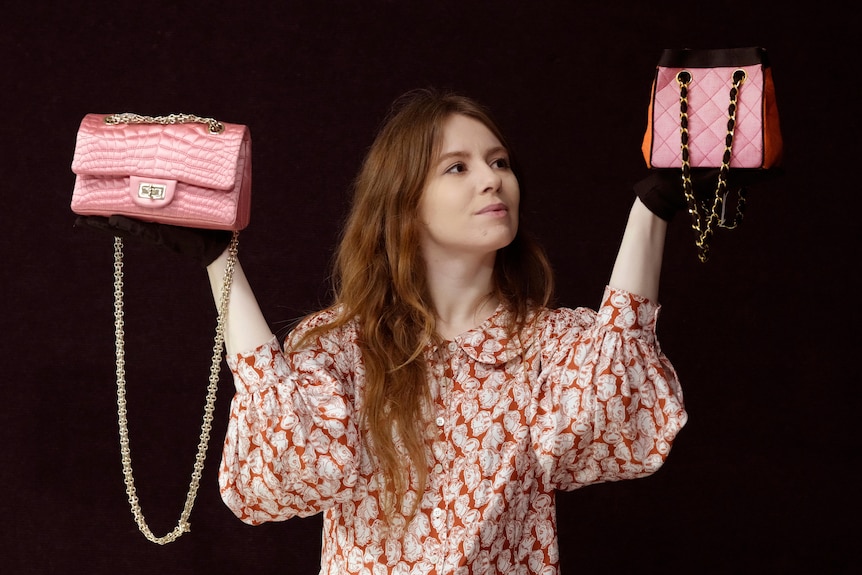 A woman holds up two pink handbags 