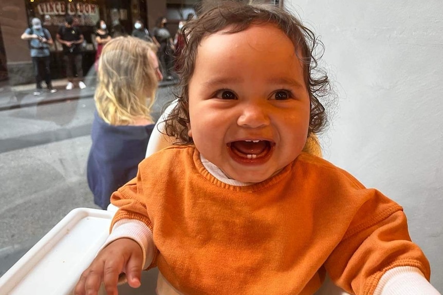 Baby Tzita Natnael  Fairfax sits in a high chair, smiling widely
