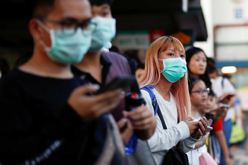 A line of commuters wearing masks waiting in a line