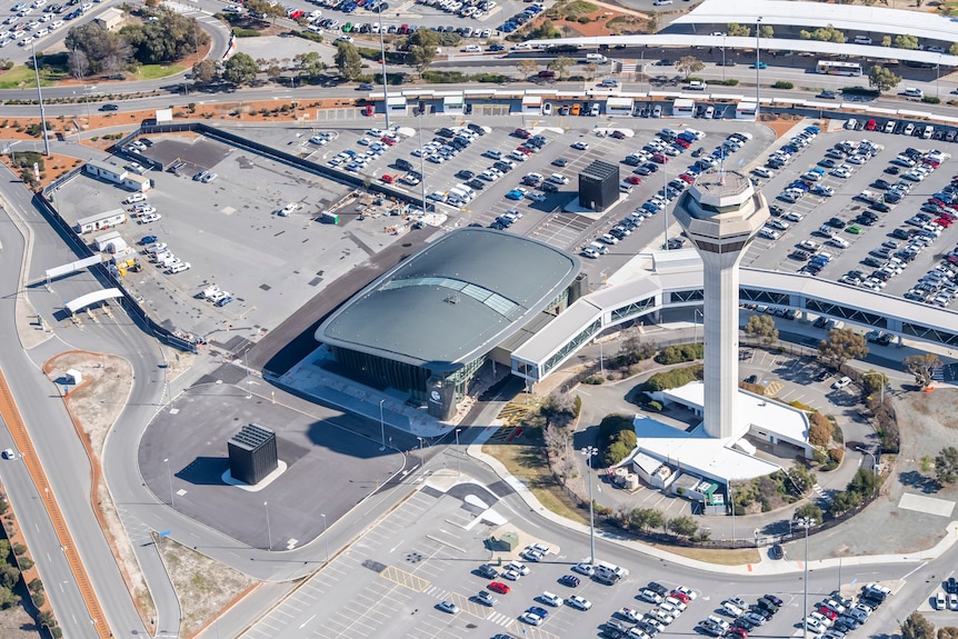 An aerial shot of a large structure right next to an air traffic control tower. 