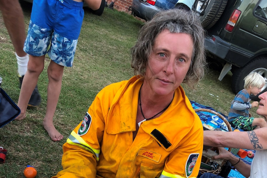 a woman sits with a cup in hand and firefighting uniform on