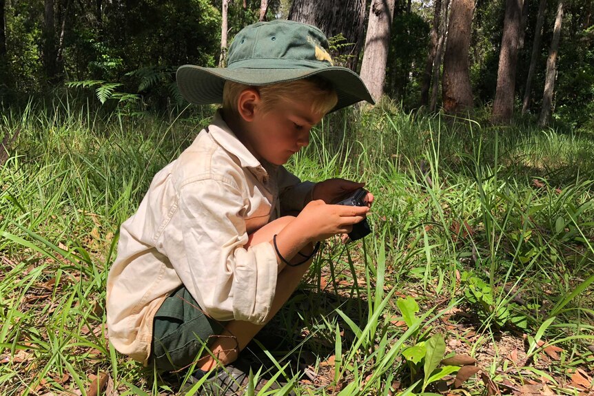 A kindergarten student at The Nature School Primary taking a photo of an insect in the grass.