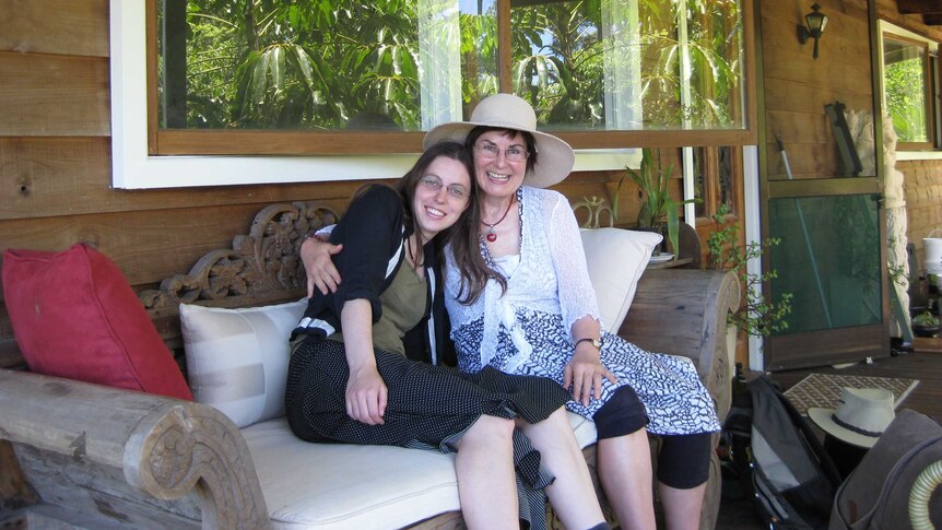 Judith McIntyre with her daughter Sarah, hugging on a chair on a verandah.