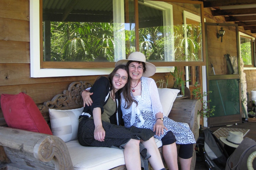 Judith McIntyre with her daughter Sarah, hugging on a chair on a verandah.
