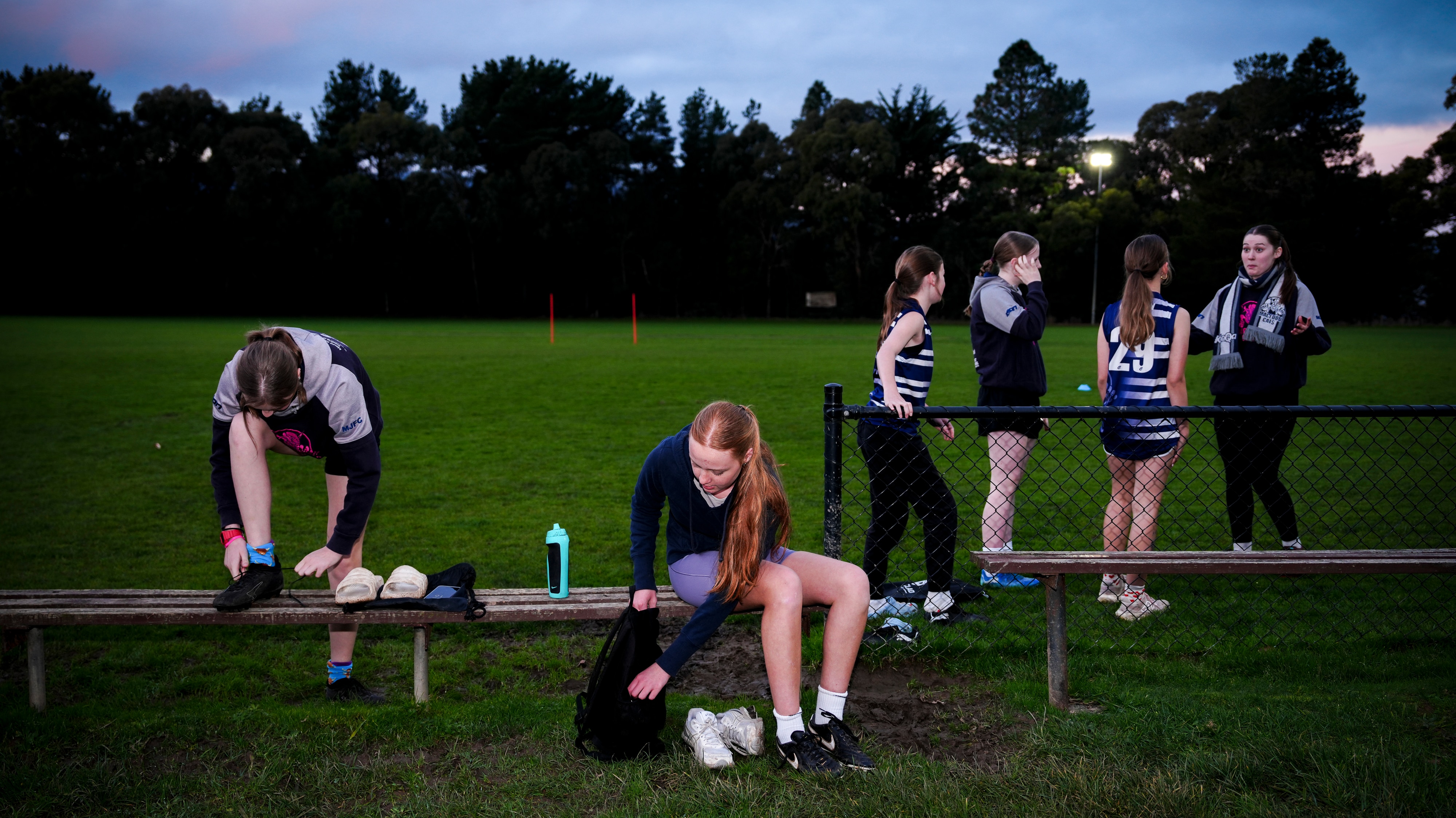 Girls players getting changed on the benches outside the football field.