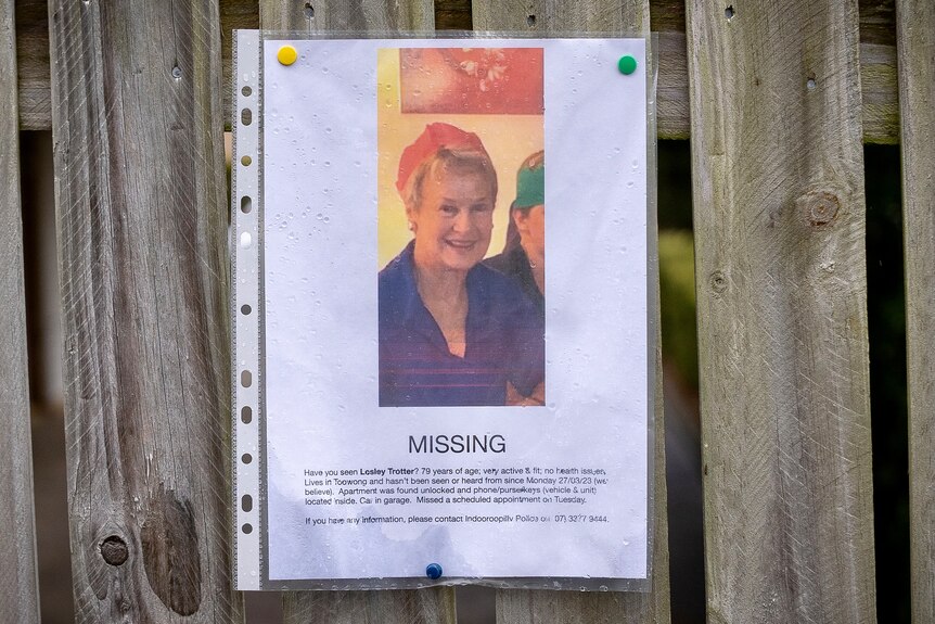 a homemade missing poster with a picture of a woman printed on white paper and thumbtacked to a fence