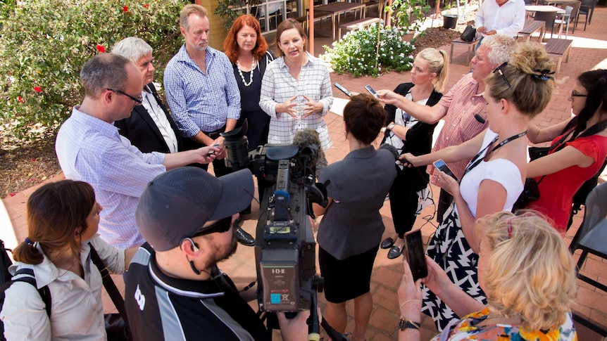 Federal Health Minister Sussan Ley talks to reporters holding cameras and microphones outdoors.