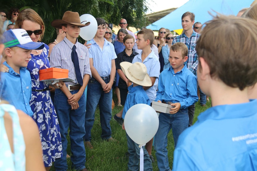 Dozens of young people and adults wear blue and look forlorn.