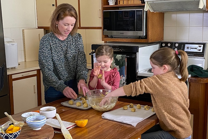 Two young children with their mother backing in a kitchen.