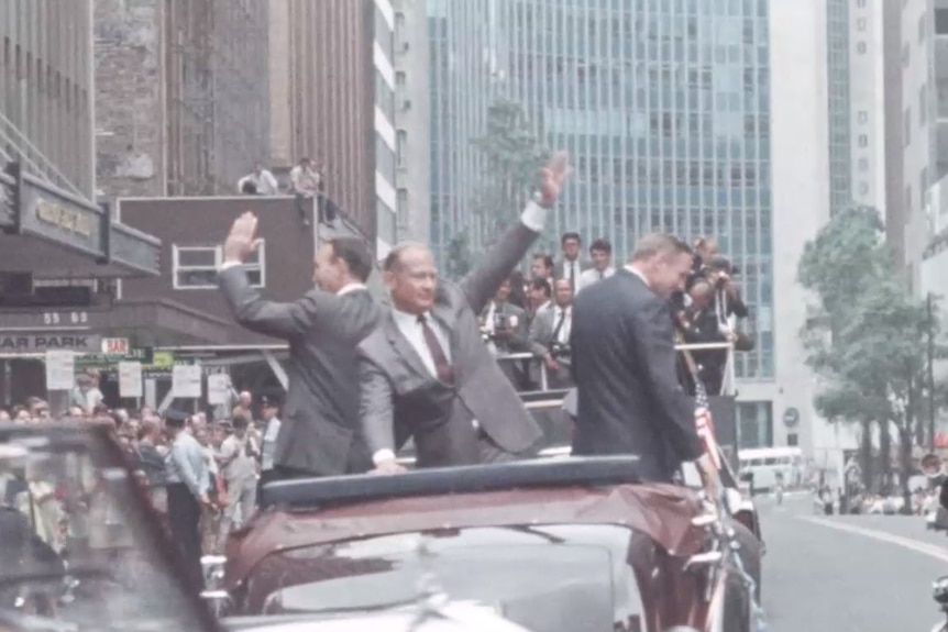 Michael Collins, Buzz Aldrin and Neil Armstrong in Sydney in a convertible, waving to crowds on either side of a road
