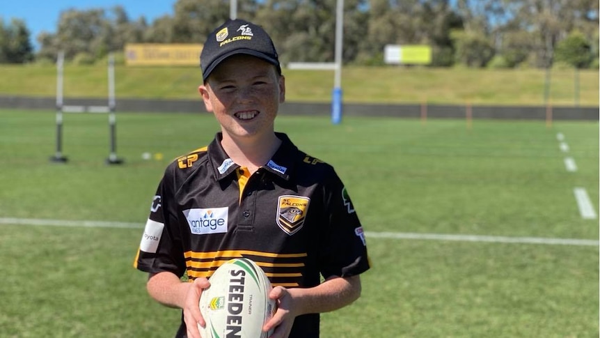 A boy in a black shirt with a cap holding a football