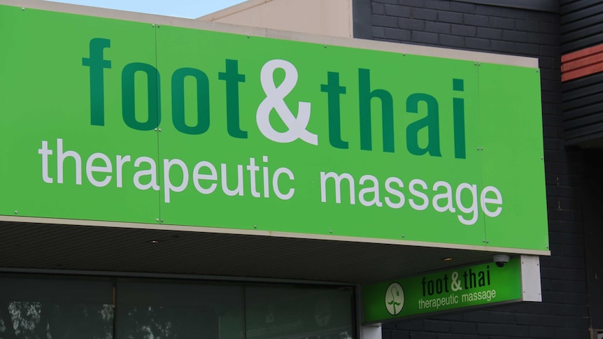 A green sign on a building reading Foot and Thai Therapeutic Massage.