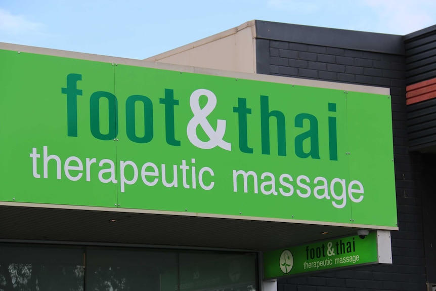 A green sign on a building reading Foot and Thai Therapeutic Massage.