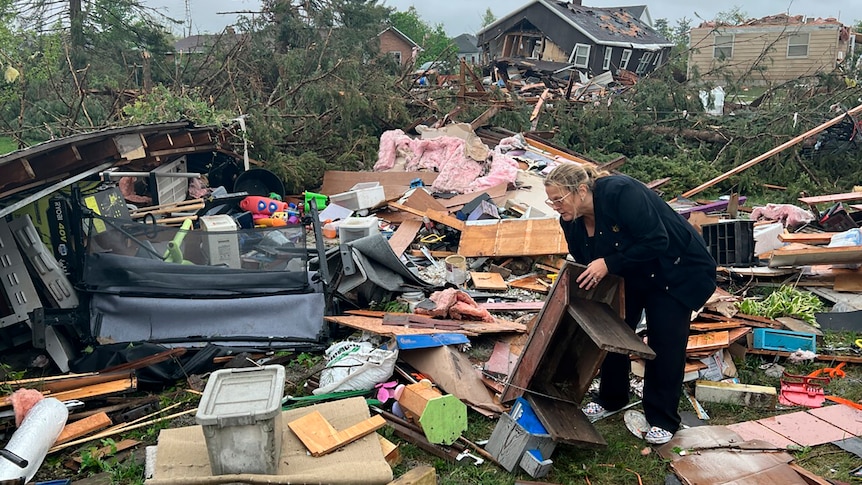 a woman sorts through broken pieces of items in her destroyed home 