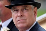 A close up of Prince Andrew wearing a suit and a top hat as he rides in a horse drawn carriage.