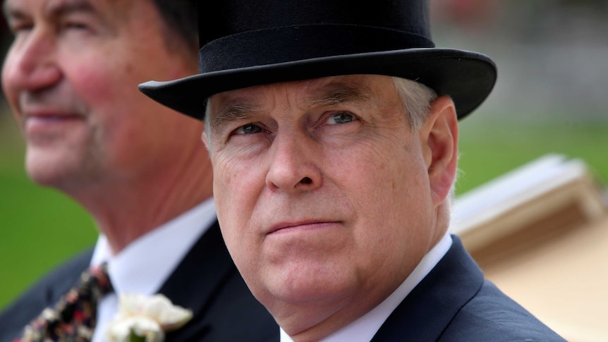 A close up of Prince Andrew wearing a suit and a top hat as he rides in a horse drawn carriage.