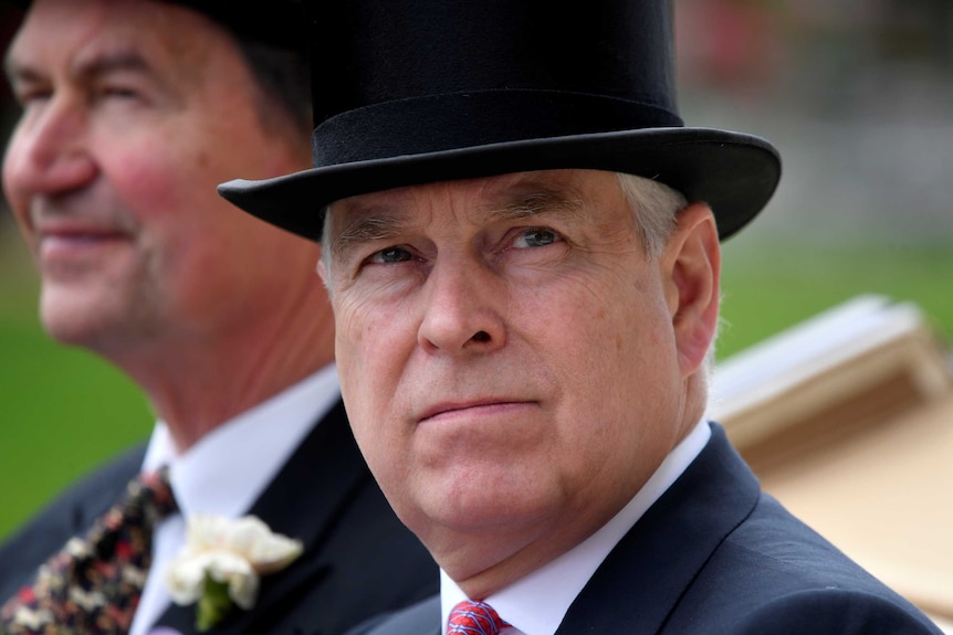 A close up of Prince Andrew wearing a suit and a top hat as he rides in a horse drawn carriage.