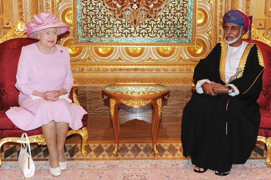 Queen Elizabeth wears a pink dress and hat, sitting next to Sultan Qaboos bin Said in an ornate room on red chairs.