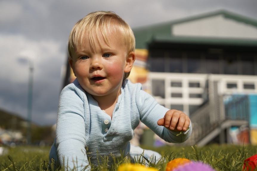 Blonde-haired toddler playing with toys on a lawn.