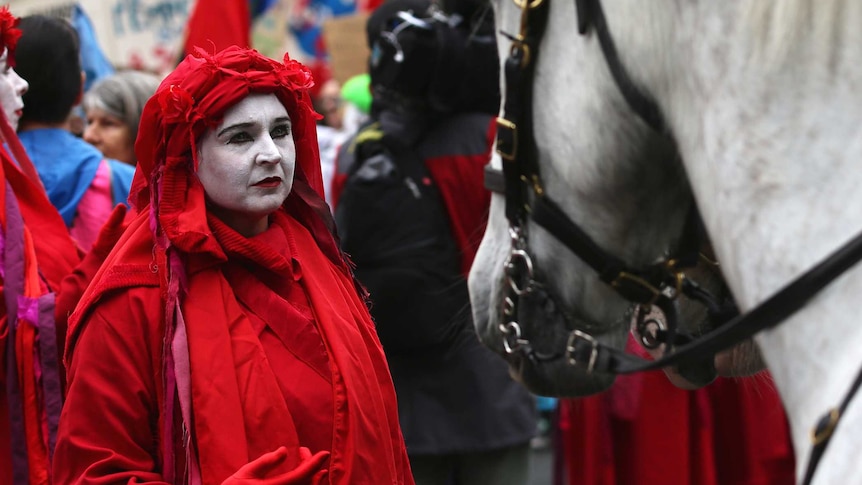 Extinction Rebellion protesters in red look at a police horse.
