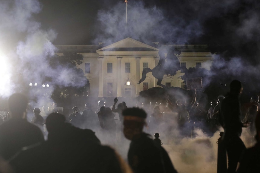 At night, you look through a crowd of black silhouettes running through smoke as the White House sits in the distance.