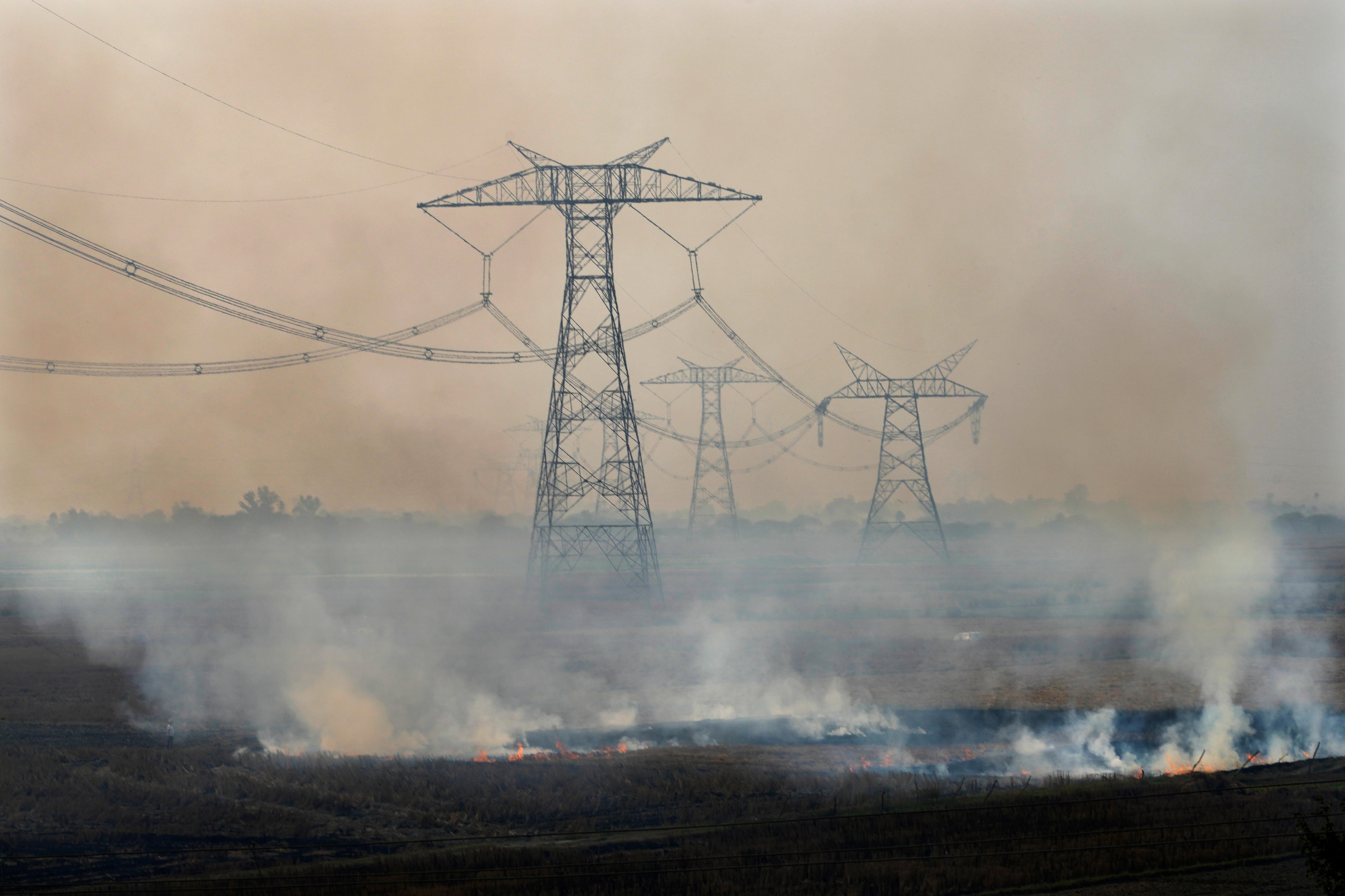 Smoke emerges from fires on the ground in front of large overheard power lines