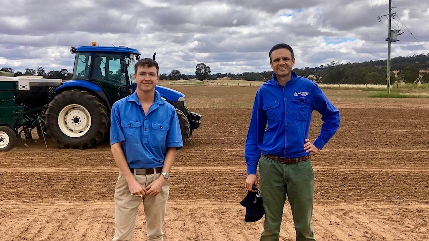 Two men standing in a harvest paddock smiling at the camera.