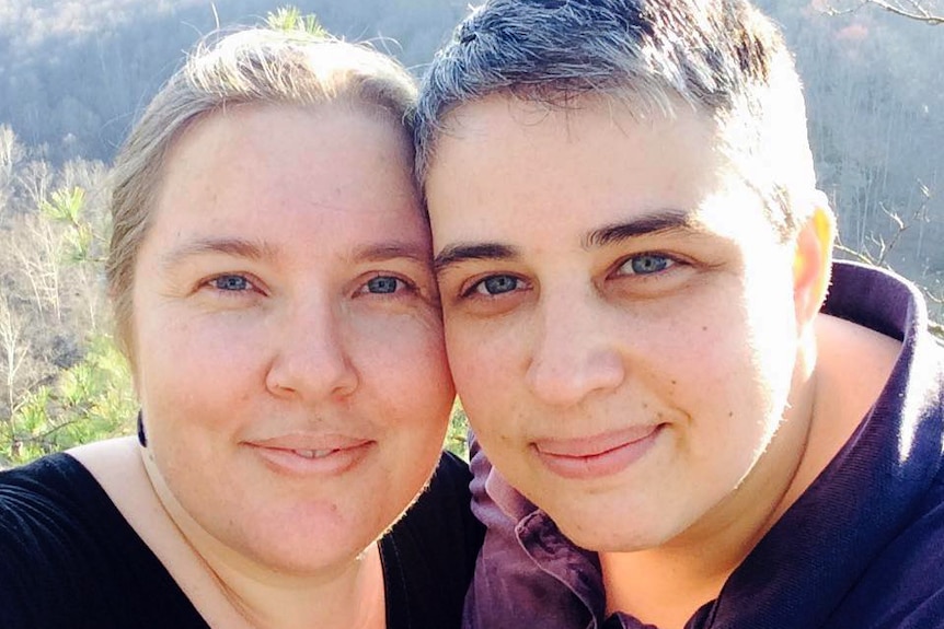 Lisa and her partner Liz pose together in a selfie in front of a wooded hill.