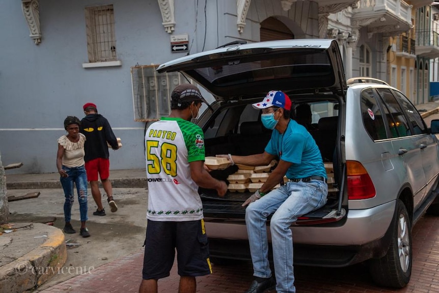 A man with a face mask on hands out food to another man on a street in Panama City.