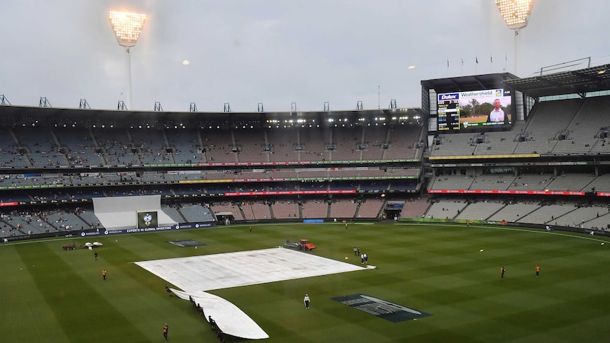 Ground crews work on the covers as rain falls at the MCG
